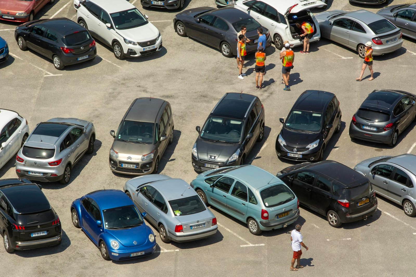 Aerial view of a crowded parking lot with various cars and people congregating.
