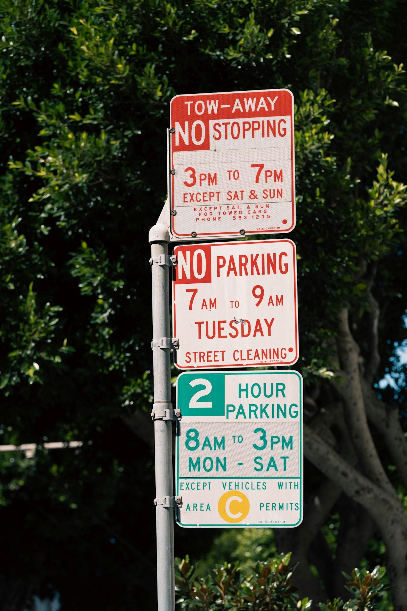 Street parking signs displaying timing and rules in a shaded urban area.